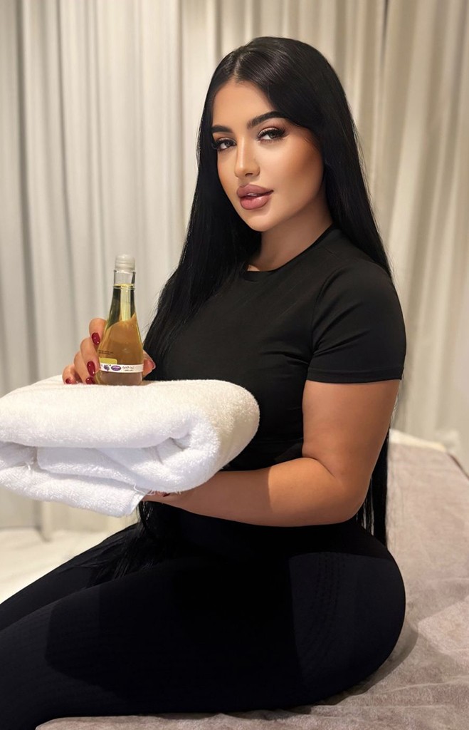 Dark-haired massage therapist with a towel and massage oil in her hands
